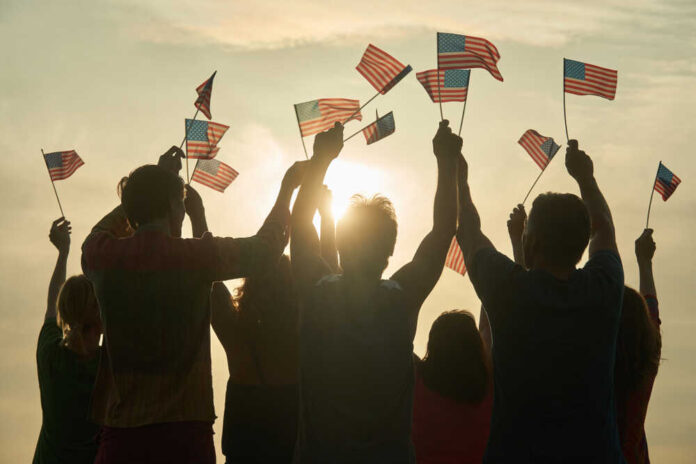 shutterstock_1175373136.jpg featured image People holding and waving American flags at sunset sky