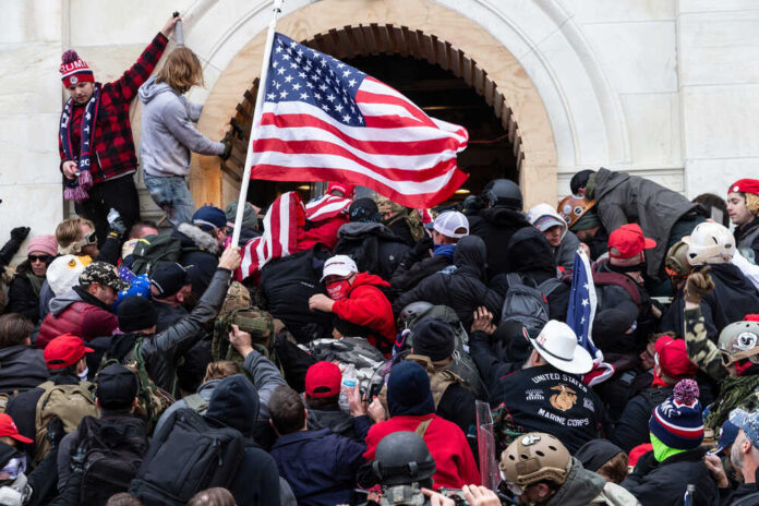 shutterstock_1889190787-1.jpg featured image Crowd storming a building, waving an American flag.