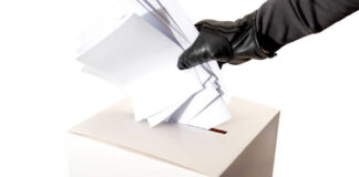 Gloved hand placing multiple papers in a ballot box.
