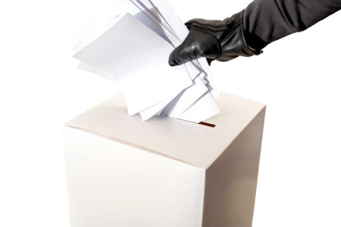 Gloved hand placing multiple papers in a ballot box.