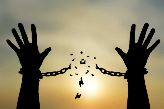 shutterstock_703687810.jpg featured image Silhouetted hands breaking chains against sunset sky.