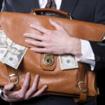 Person clutching leather bag with money sticking out.
