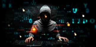 Hacker in dark room with code on screen.