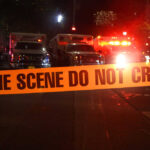 Crime scene tape with emergency vehicles in background.