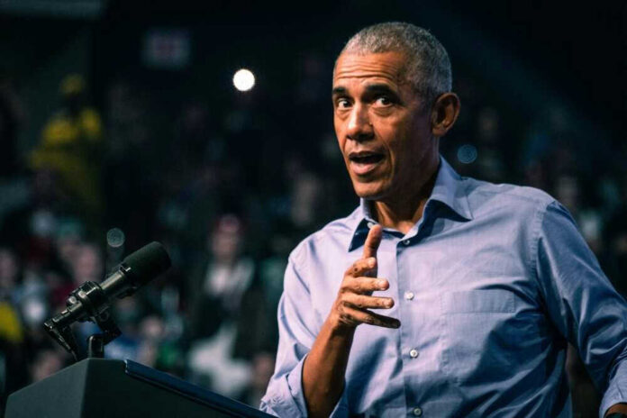 Barack Obama in blue shirt speaking at podium with microphone