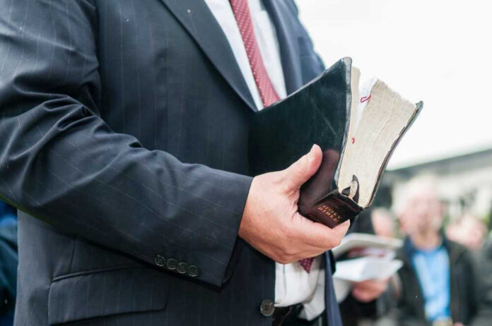shutterstock_2396099421.jpg Man in suit holding a worn Bible