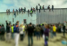 People sitting on a border wall with crowd below