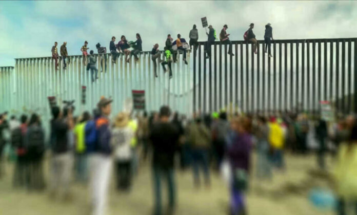 People sit atop a border wall during protest