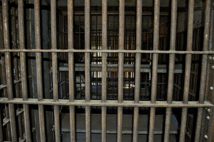 Empty, rusty barred jail cell with metal bunks