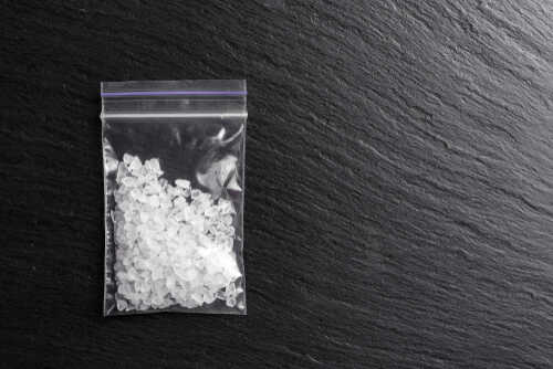 White crystals drugs methamphetamine in a plastic bag on a black background