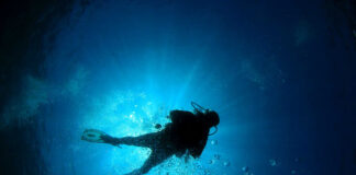Scuba diver underwater with sun rays filtering through.