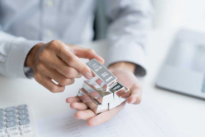 Person holding silver bars in hand with a calculator and documents on the table