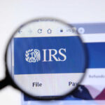 Massive IRS Cuts: Tax Season Nightmare? Magnifying glass focusing on IRS website logo.
