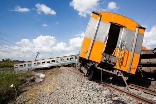Derailed train car leaning off the tracks with another train in the background