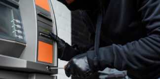 A person in a black hoodie and gloves tampering with an ATM
