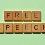 Senator Sues Defense Chief: Free Speech War Erupts Wooden letter tiles spelling 'FREE SPEECH' on a light green background