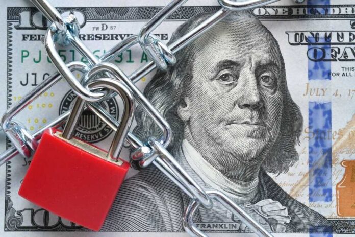 A red padlock and chain over a hundred dollar bill featuring Benjamin Franklin