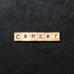 SHOCKING Cancer-Alzheimer’s Connection — DETAILS Wooden letters spelling the word 'Cancer' on a black textured background