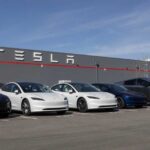 A lineup of Tesla cars parked in front of a Tesla building