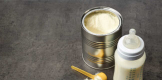 A can of powdered baby formula next to a feeding bottle with milk