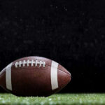 Ex-NFL Star ARRESTED — Murder!? Close-up of a football on a grassy field.