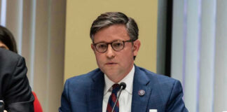 Mike Johnson in a suit speaks into a microphone.