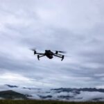 A drone flying against a cloudy sky over a mountainous landscape