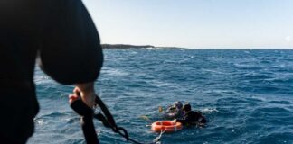 Two scuba divers in the ocean being assisted by a person holding a rescue line