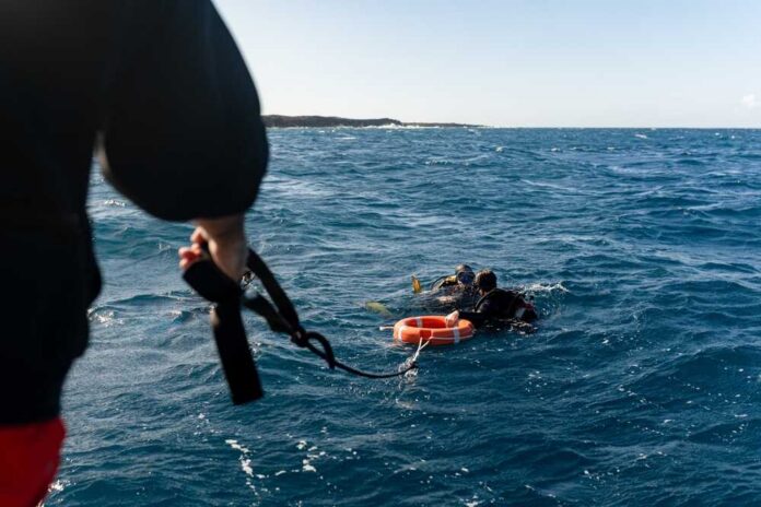 Two scuba divers in the ocean being assisted by a person holding a rescue line