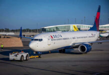 Delta airplane being towed at airport terminal gate.