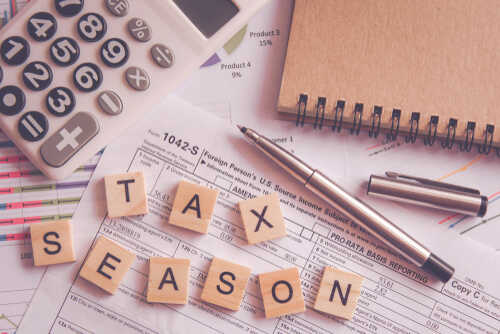 Calculator and tax documents with wooden letters spelling 'TAX SEASON'