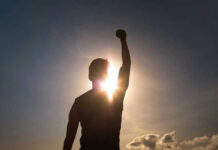 Silhouette of person with raised fist against sunset.