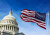 US Capitol with American flag waving in foreground.