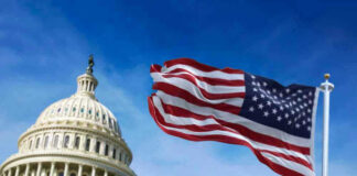 US Capitol with American flag waving in foreground.