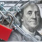 A red padlock and chain over a hundred dollar bill featuring Benjamin Franklin
