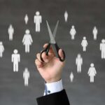 BRUTAL Cuts Coming to Social Media Giant A hand holding scissors with icons of people in the background