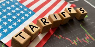 Wooden blocks spelling 'TARIFFS' on a background of the US flag and financial charts