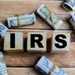 IRS Policy Change BLOCKS Millions from Tax Money Wooden blocks spelling IRS surrounded by rolled currency notes