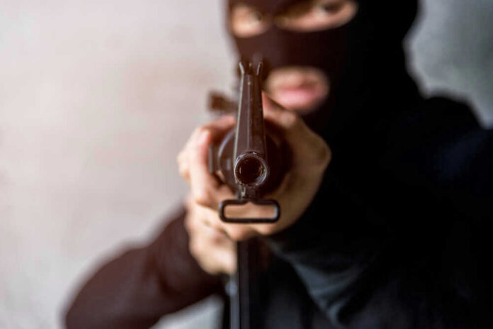 shutterstock_747936787.jpg Person in balaclava aiming rifle at the camera.