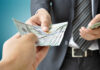 A person handing over a stack of cash to another individual in a suit