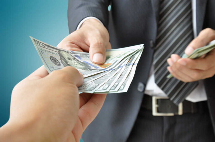A person handing over a stack of cash to another individual in a suit