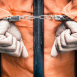 Ten Killers Escape — Sheriff Now Faces PRISON! Handcuffed person in orange jumpsuit behind prison bars.