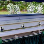 A casket at a graveside surrounded by floral arrangements
