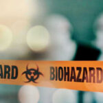 Contamination Crisis Rocks Popular Chocolate Maker Biohazard tape with blurred figures in background.