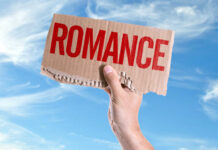 A hand holding a cardboard sign that reads 'ROMANCE' against a blue sky