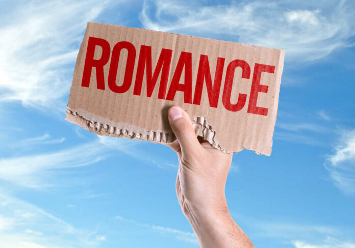 A hand holding a cardboard sign that reads 'ROMANCE' against a blue sky