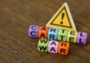Colorful letter blocks spelling 'CARTEL' and 'WAR' with a warning sign