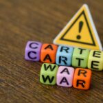 Colorful letter blocks spelling 'CARTEL' and 'WAR' with a warning sign