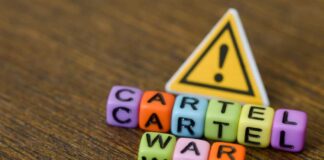 Colorful letter blocks spelling 'CARTEL' and 'WAR' with a warning sign