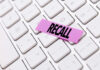 A pink sticky note with the word 'RECALL' placed on a white keyboard